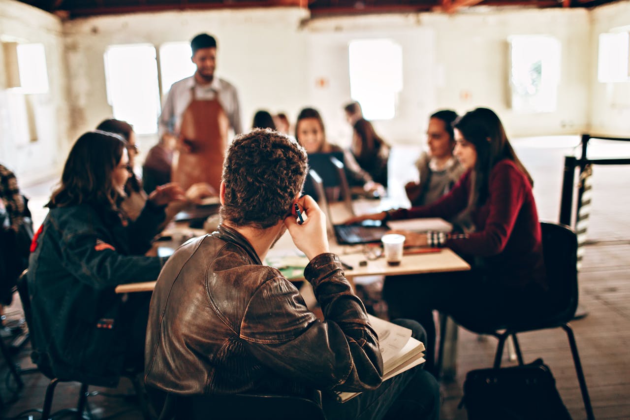 Group of diverse coworkers with laptops and papers gathering at table in shabby building with male server helping with snacks during business discussion